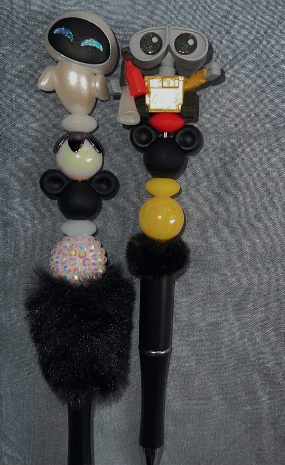 Two robot-themed handmade pens with black, white, red, and yellow bead stacks.