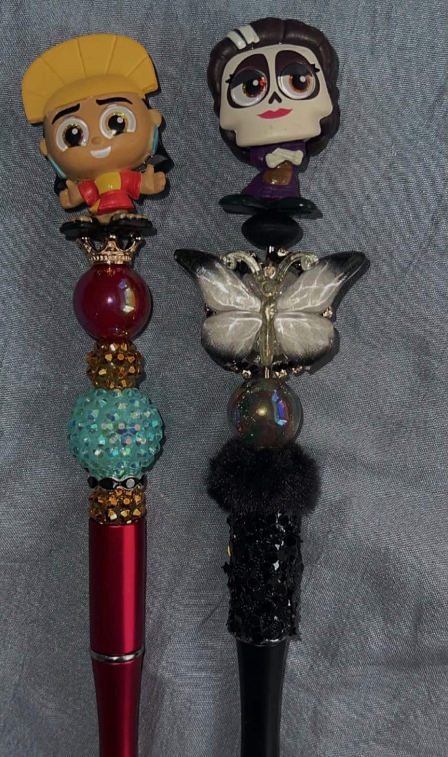 Two dramatic pens in dark tones with butterfly, crystal, and plush accents.